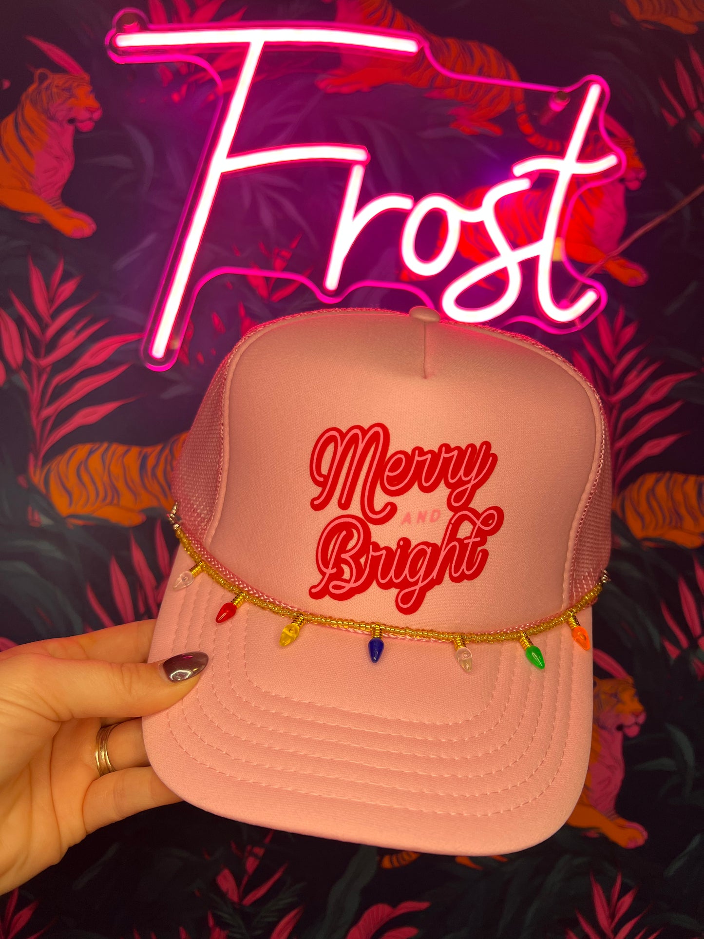 Light pink foam trucker hat with “Merry & Bright” design and Christmas light chain accessory — holiday hat from Frost Impressions Boutique in Wapakoneta, Ohio.