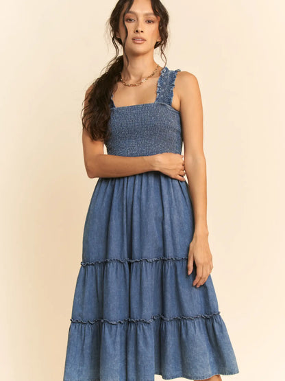 Washed denim midi dress with smocked bodice, adjustable straps, and tiered skirt design