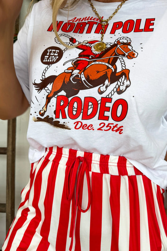 Cowgirl Christmas Graphic Tee — North Pole Rodeo design featuring Santa riding a reindeer, relaxed fit holiday tee from Frost Impressions Boutique in Wapakoneta, Ohio.