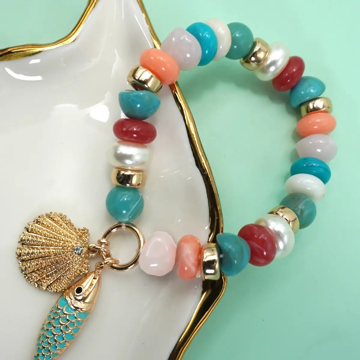 Gold beaded stretch bracelet with fish charm, seashell detail, and pearl accents in coastal beach style