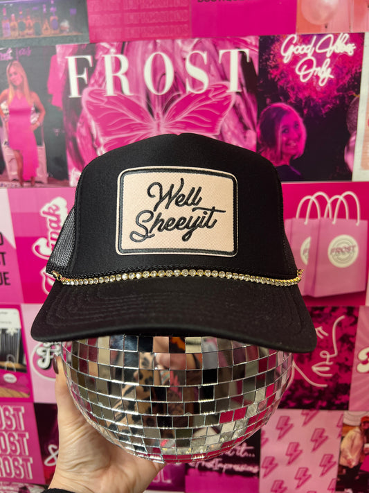 Black trucker hat with “Well Sheeyit” patch and silver hat chain — bold boutique fashion accessory.