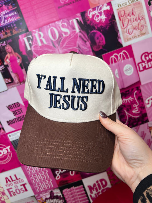 Brown front trucker hat with navy puff embroidery reading “Y’all Need Jesus” — 5-panel snapback style.