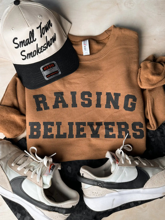 Raising Believers Crewneck — pecan-colored Jerzees sweatshirt with varsity-style faith graphic from Frost Impressions Boutique in Wapakoneta, Ohio.